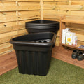 Two black plastic planters against a wooden wall with gardening supplies.