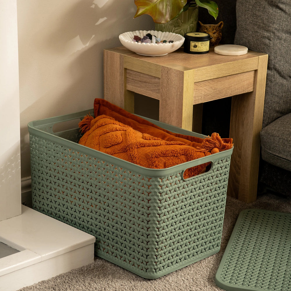 Plastic Box Shop extra large sage green storage basket with lid, textured weave design, holding orange blankets.